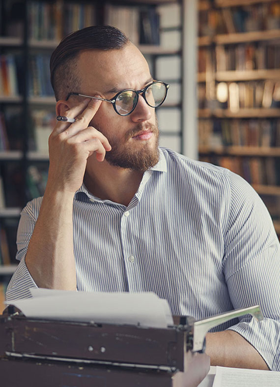 A man in glasses sitting at a desk with a typewriter, focused on his work, representing eBook writing services.