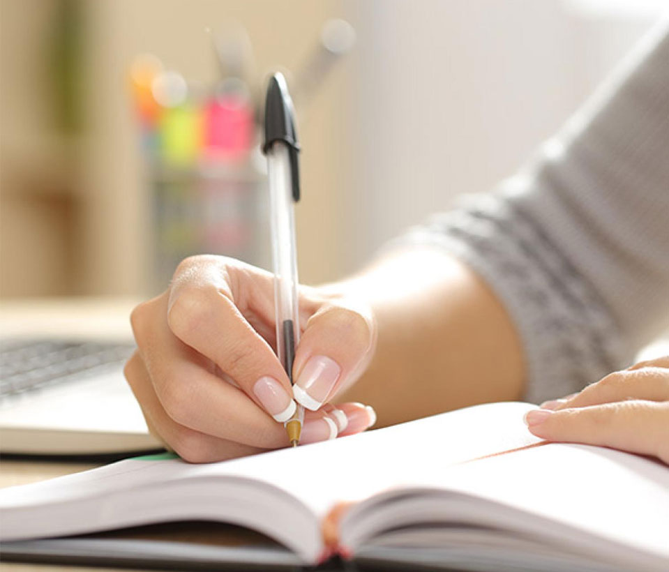 A person diligently writing books in a notebook with a pen, capturing their thoughts.