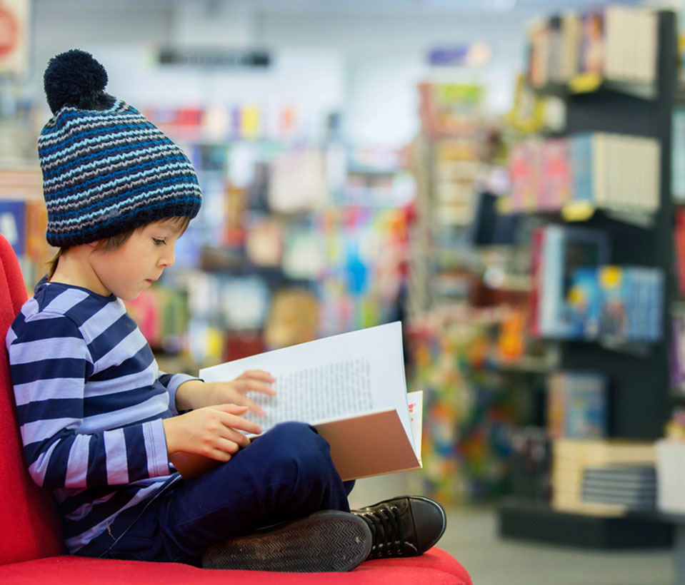 A young boy reads a limited edition children's book while seated on a vibrant red chair.