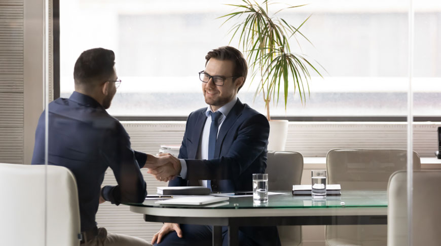 Two men shaking hands at a meeting table, collaborating on book editing and publishing services.