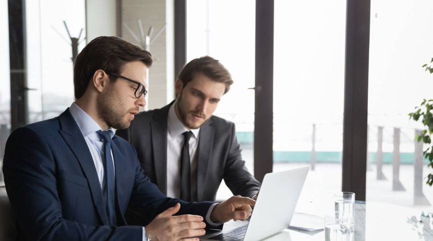 Two businessmen in suits collaborating at a table with a laptop, focusing on book editing and publishing services.