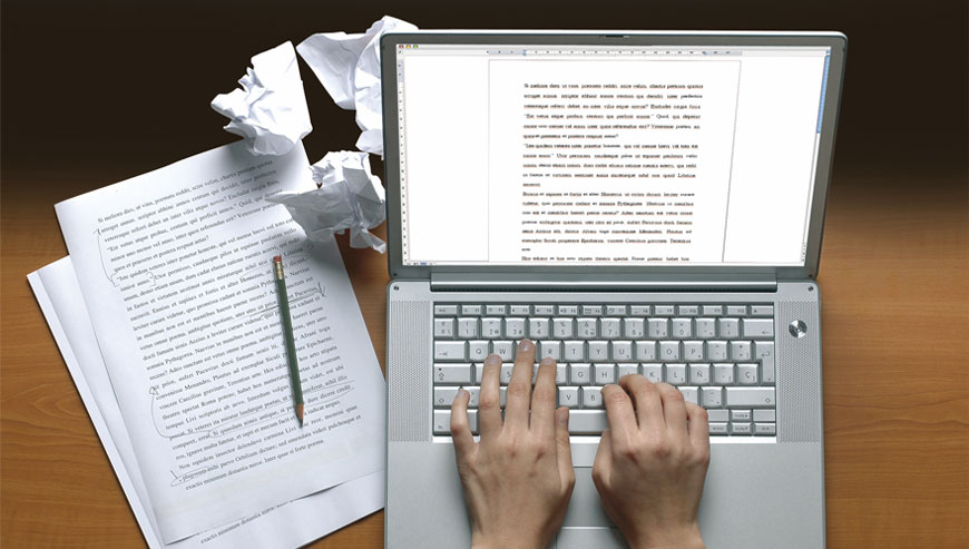 A person typing on a laptop surrounded by papers and a pen, illustrating an ebook conversion service in action.