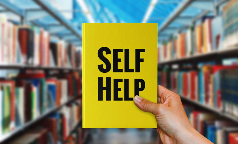 Individual grasping a self-help book in a library setting, showcasing shelves filled with self-help ebooks around them.