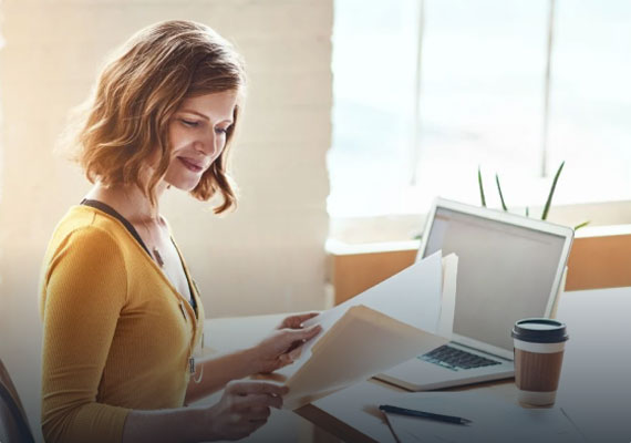 A woman working at a desk with a laptop and papers, focusing on proofreading services for authors.