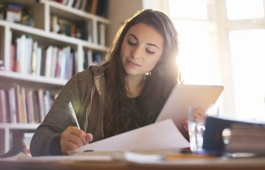 A girl sitting at a desk, using a tablet and pen to create illustrations for eBook writing services.
