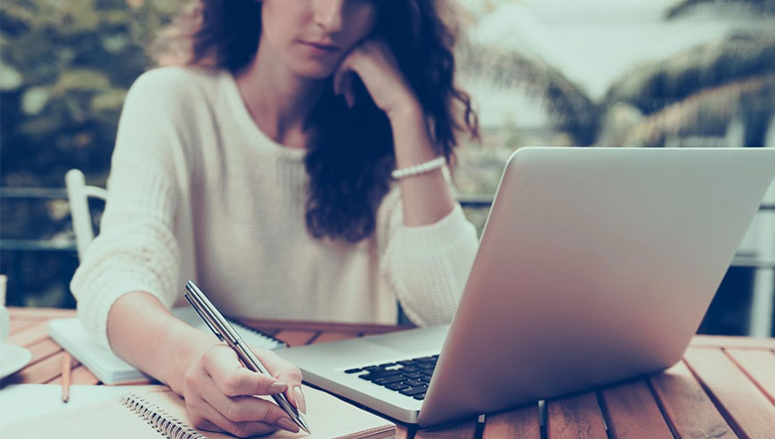 A woman at a table with a laptop and pen, providing unique ebook writing services with focus and creativity.
